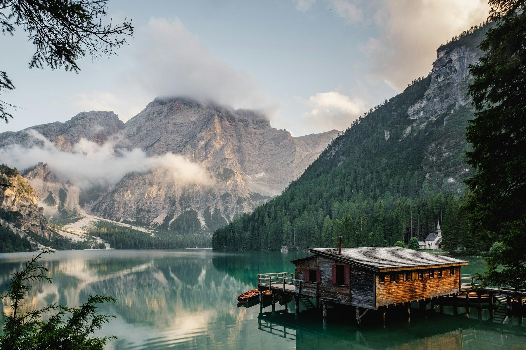 A brown house on a still alpine lake at dusk. Photo by Luca Bravo on Unsplash.
